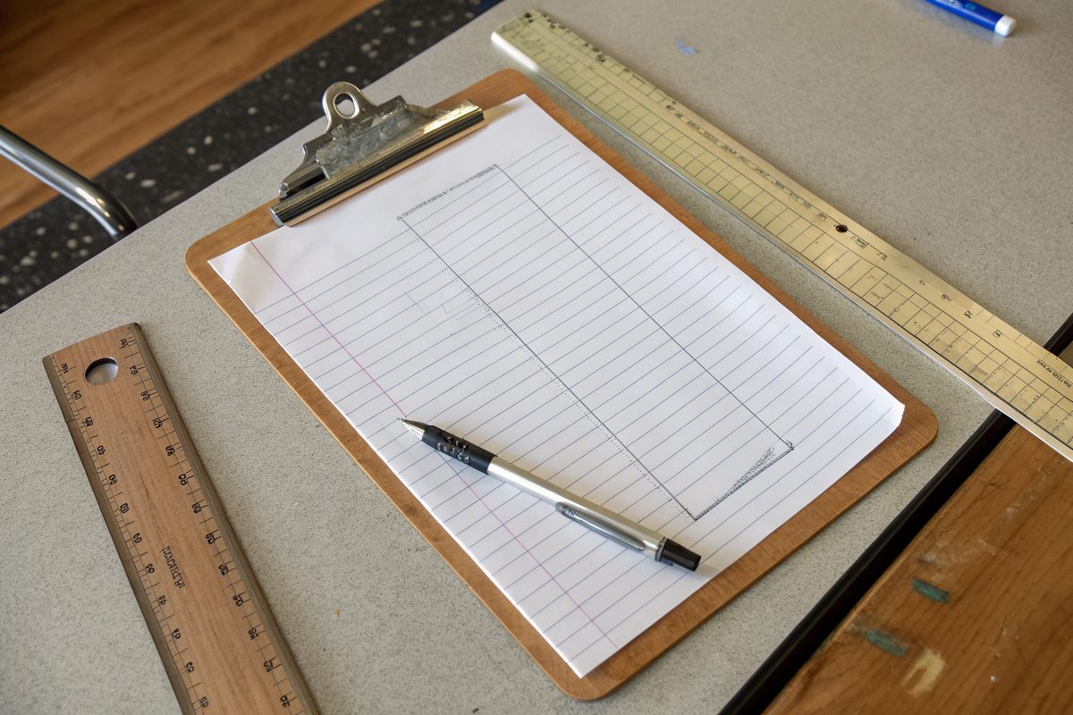 A clipboard with a simple floor sketch, a pen and rulers on a table