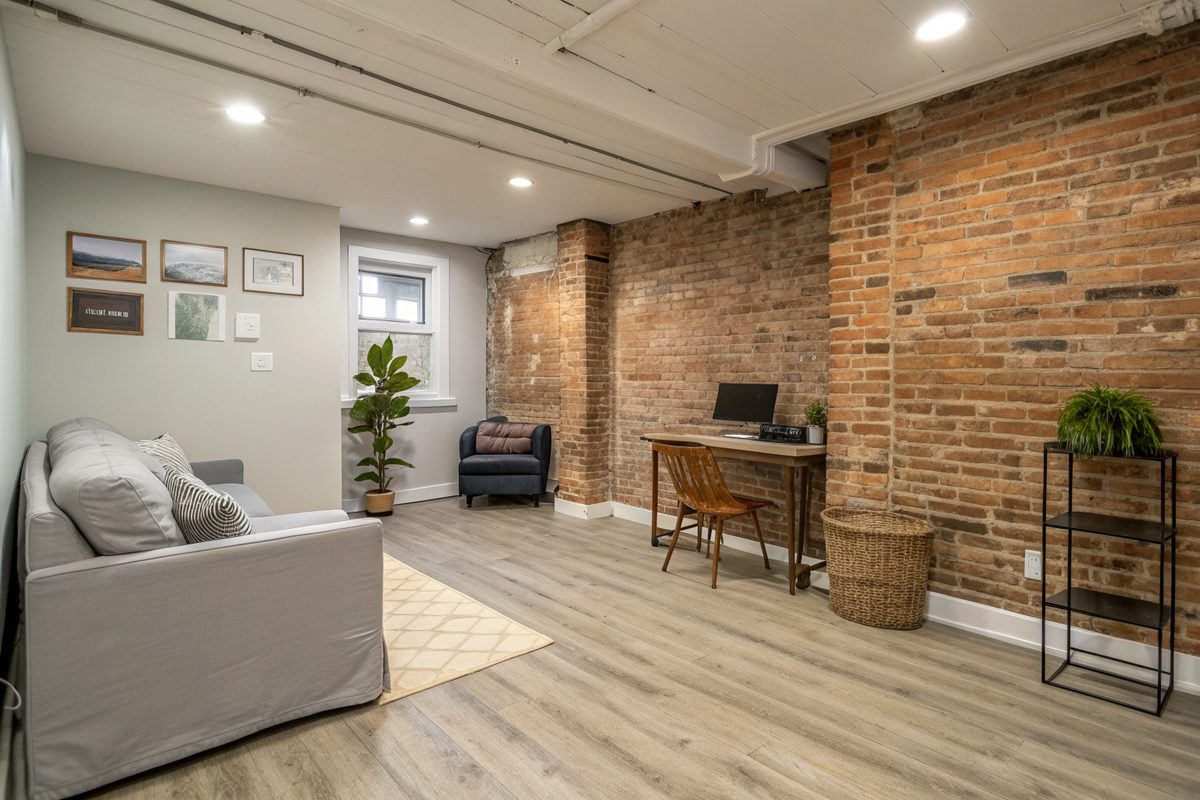 A dry finished rowhouse basement with an exposed brick wall, a sofa and a desk